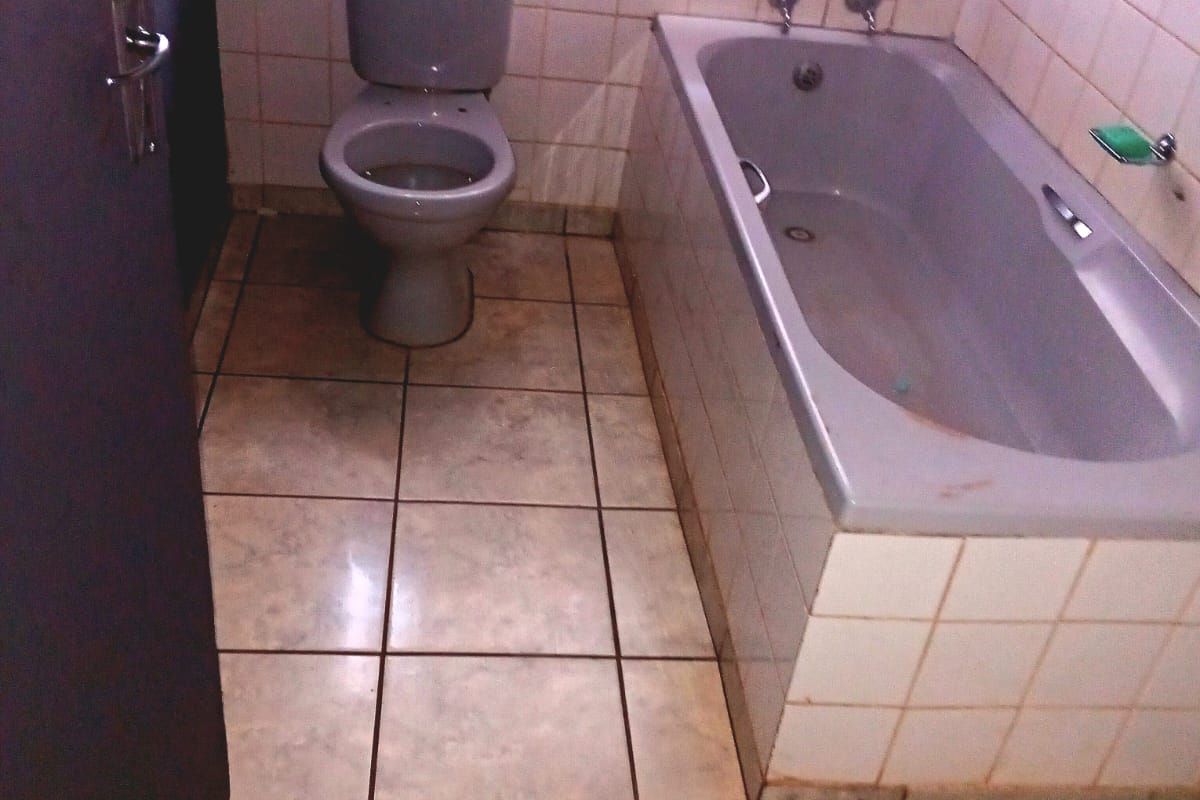 A functional bathroom featuring a built-in bathtub and toilet with tiled finishes, requiring cosmetic updates to improve its overall condition and appeal.