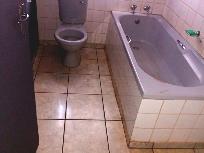 A functional bathroom featuring a built-in bathtub and toilet with tiled finishes, requiring cosmetic updates to improve its overall condition and appeal.