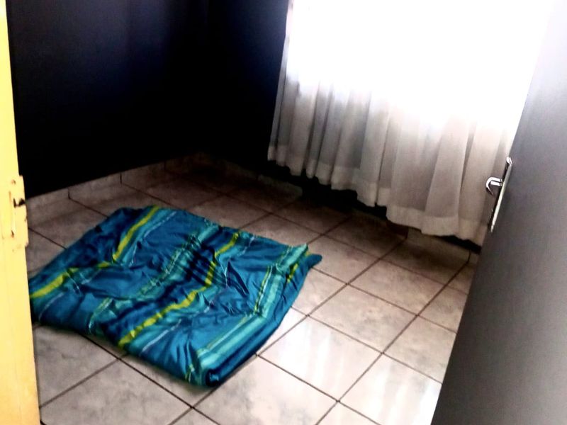 A small, empty bedroom featuring tiled flooring and dark painted walls, currently vacant and awaiting new furnishings.