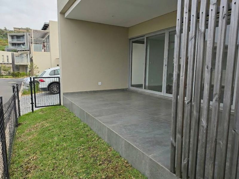 A modern covered patio featuring large format floor tiles, sliding glass doors, and a wooden privacy screen, overlooking a small garden area.