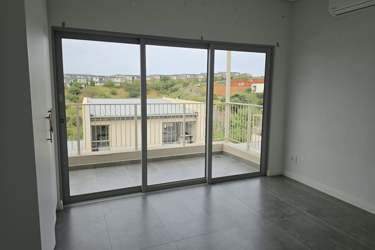 An empty bedroom featuring large sliding glass doors that open onto a private balcony with scenic views and modern tiled flooring.