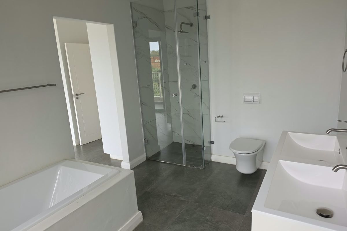Modern bathroom featuring a double vanity, wall-mounted toilet, glass-enclosed shower, and a built-in bathtub with contemporary grey floor tiles.