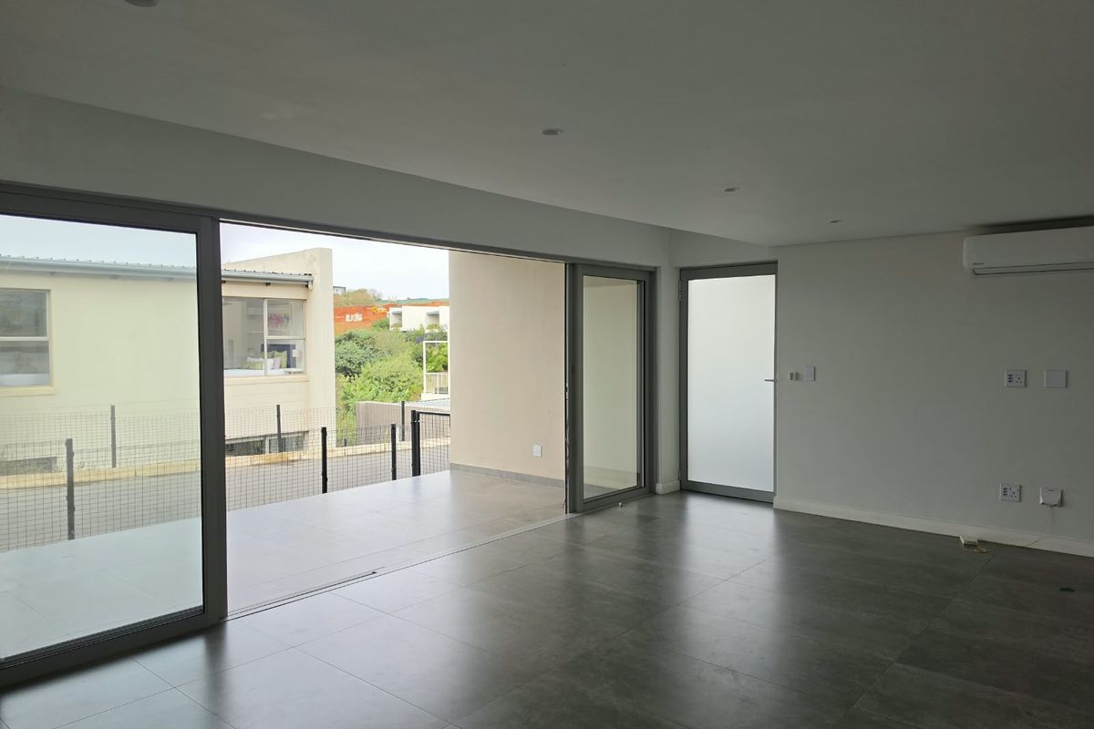 Spacious, empty living area featuring large sliding glass doors that open onto a private patio, complemented by modern tiled floors and integrated air conditioning.