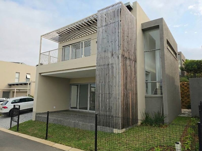 Modern townhouse exterior featuring a distinctive timber slat screen, covered ground-floor patio, upper-level balcony, and large glass windows for natural light.