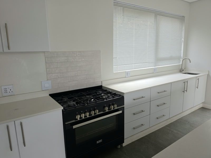Modern kitchen featuring white cabinetry, stone countertops, a black gas stove with oven, and a subway tile backsplash with a large window.