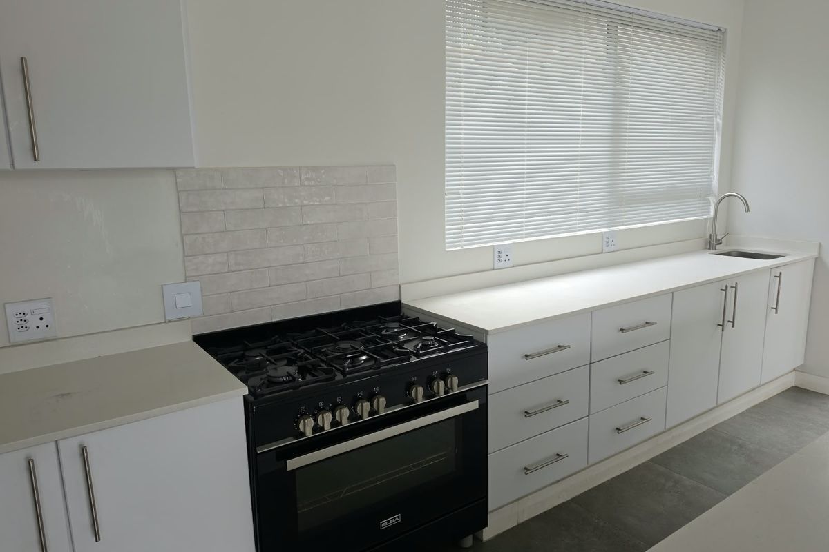 Modern kitchen featuring white cabinetry, stone countertops, a black gas stove with oven, and a subway tile backsplash with a large window.