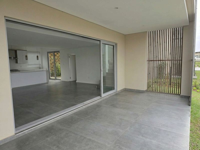 A modern covered patio featuring large format grey floor tiles, a timber privacy screen, and seamless access to the open-plan interior living area.