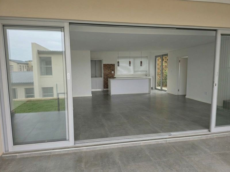 Spacious open-plan living and kitchen area featuring large sliding doors, modern tiled floors, a central island, and an exposed brick accent wall.