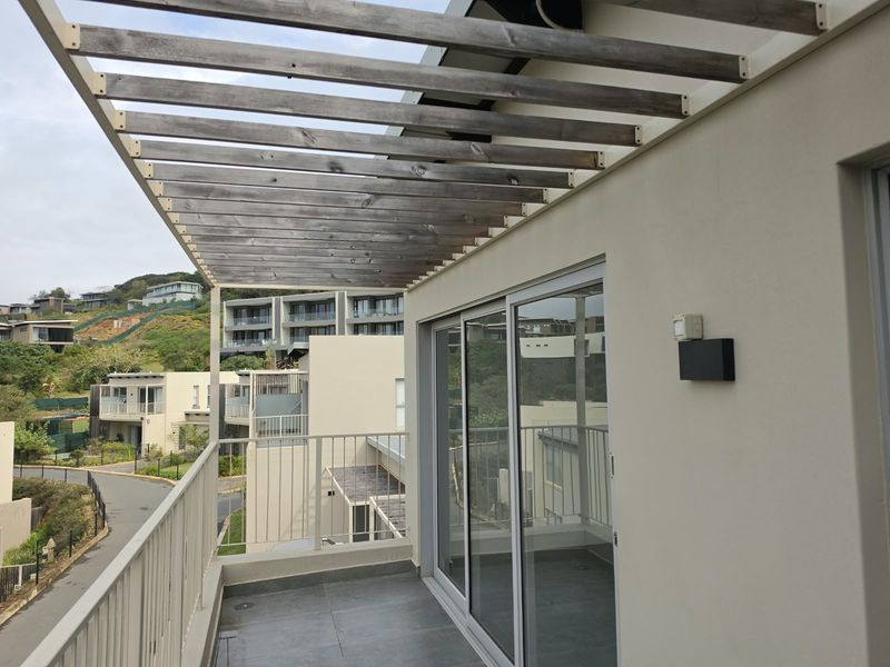 A balcony featuring a wooden pergola, tiled flooring, and metal balustrade, offering views of the surrounding residential estate.