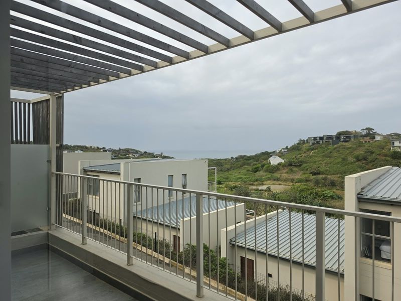 A covered balcony featuring a timber pergola and metal balustrade, offering elevated views of the surrounding landscape and distant ocean.
