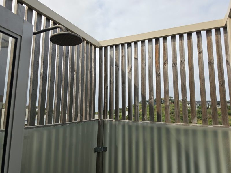 An outdoor shower area featuring a modern rainfall showerhead, frosted glass privacy screen, and timber slat enclosure.