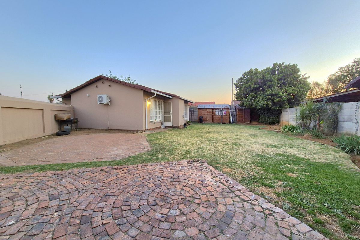 Rear view of the property featuring a brick paved patio area, a lawn, and perimeter walling.