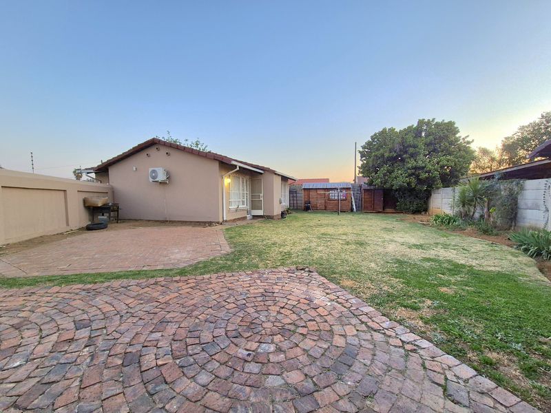 Rear view of the property featuring a brick paved patio area, a lawn, and perimeter walling.