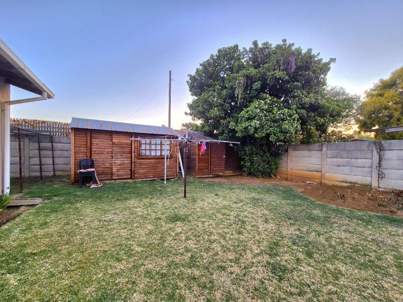 A rear garden area featuring a lawn, a wooden storage shed with a corrugated metal roof, and precast concrete boundary walls.
