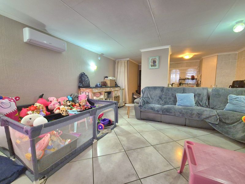 Open-plan living area featuring tiled flooring, coved ceilings, and a wall-mounted split-system air conditioner, providing a functional and versatile space.