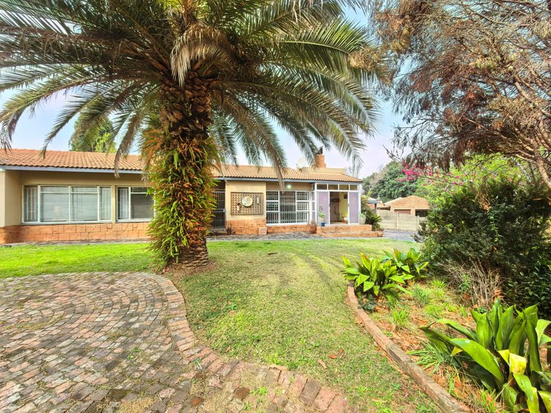 Rear view of a single-story brick house featuring a paved driveway, established garden, and security gates on the windows and doors.