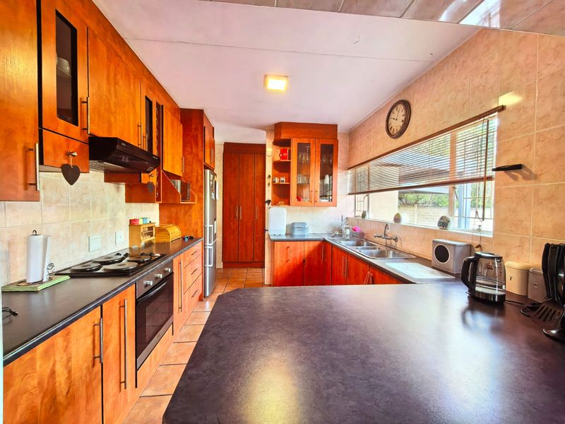 A functional kitchen featuring warm-toned wooden cabinetry, dark laminate countertops, a built-in oven with hob, and a tiled backsplash with ample storage space.