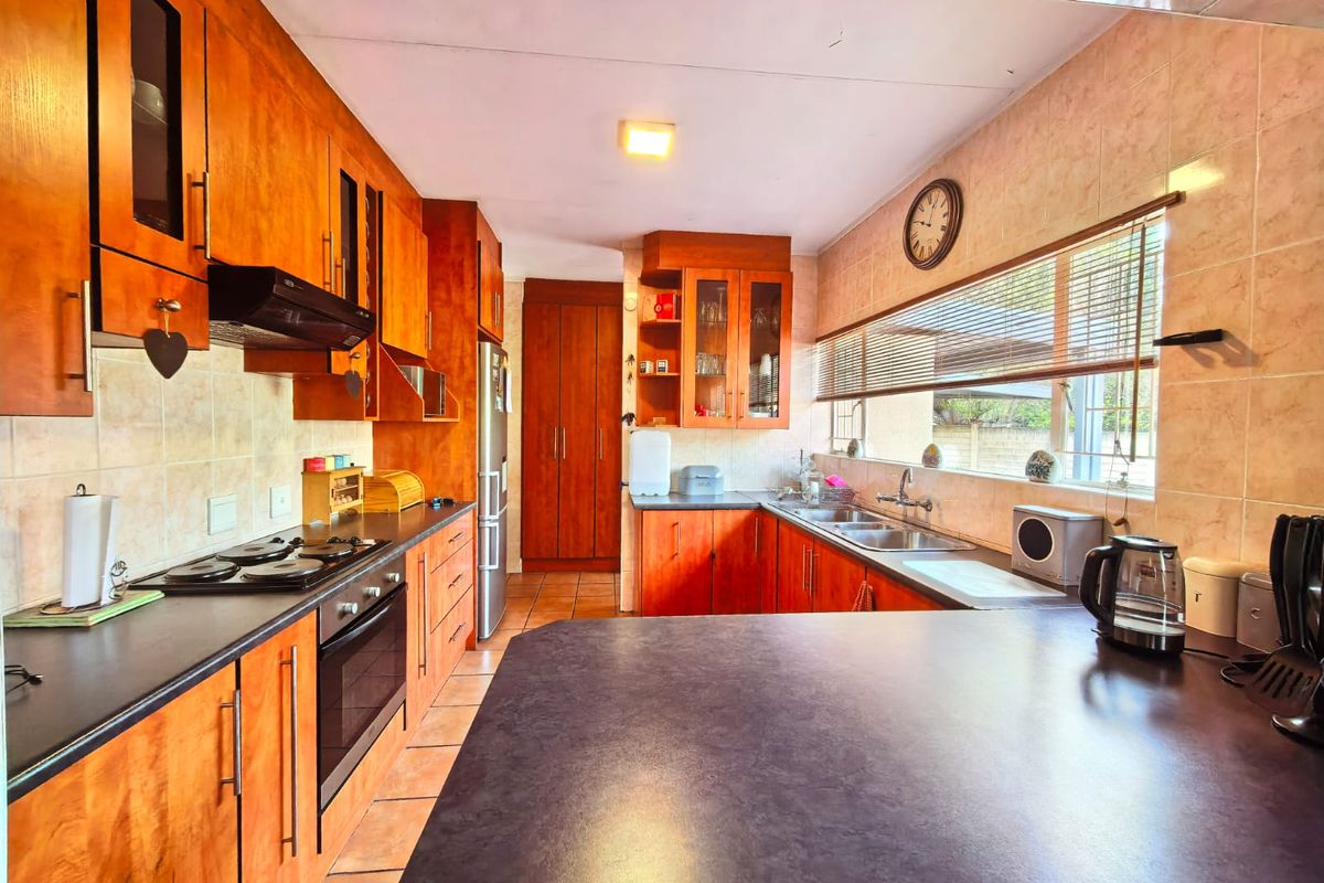 A functional kitchen featuring warm-toned wooden cabinetry, dark laminate countertops, a built-in oven with hob, and a tiled backsplash with ample storage space.