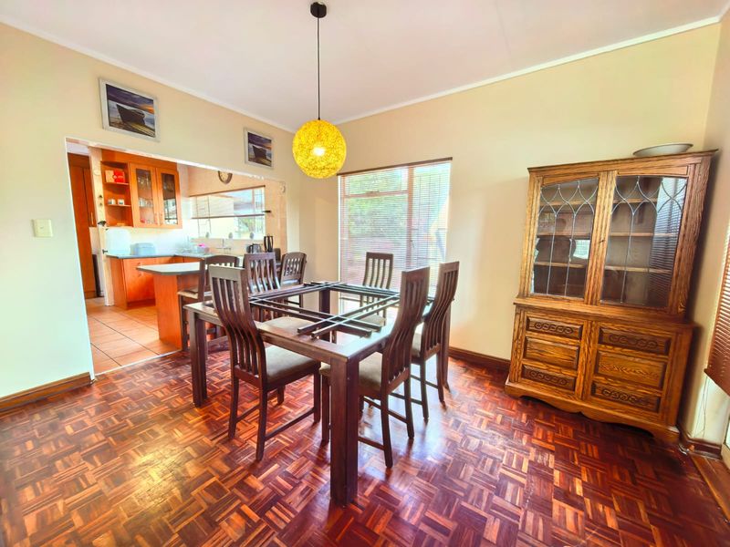 Open plan dining area featuring classic parquet flooring, flowing into a functional kitchen with built-in cabinetry and a breakfast peninsula.