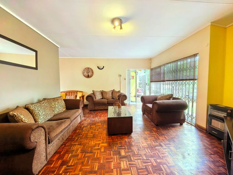 Spacious living room featuring classic parquet flooring, large windows with security gates, and direct access to an outdoor patio area.