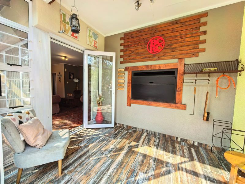 Covered patio area featuring a built-in braai, decorative timber wall cladding, and durable tiled flooring, providing seamless access to the interior living space.