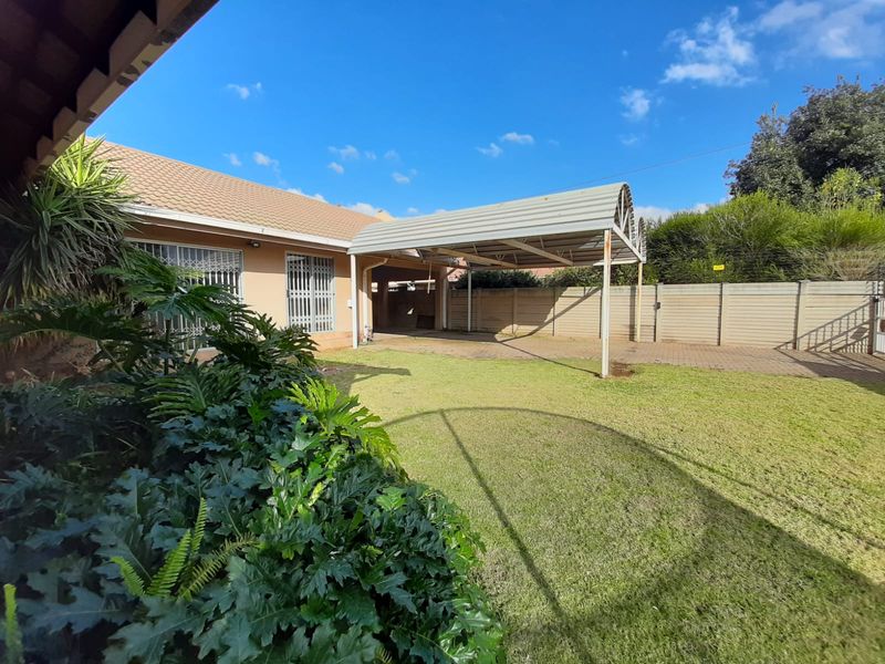Rear garden area featuring a paved driveway, a metal carport structure, and secure perimeter walling.