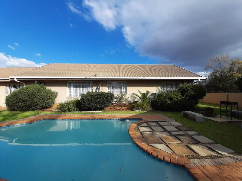 Rear view of the property featuring a swimming pool, paved surround, and established garden area with a tiled roof building facade.