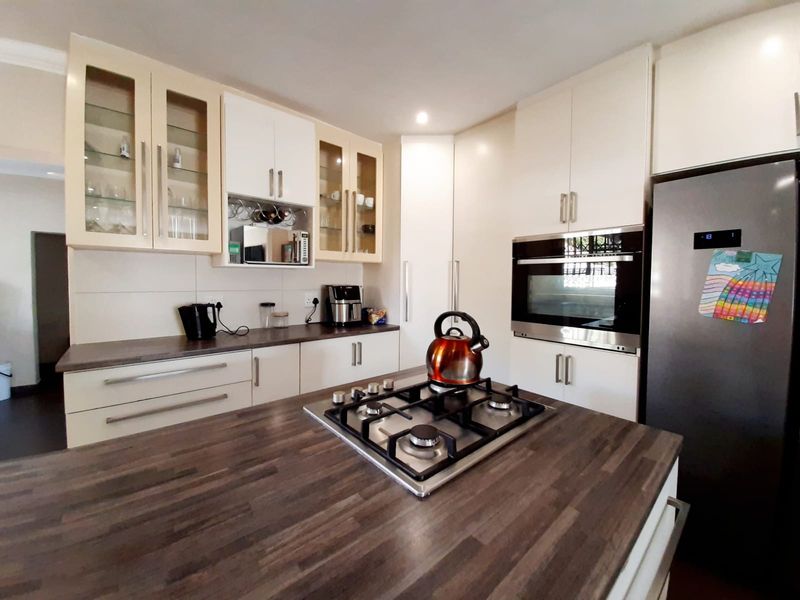 Modern kitchen featuring dark wood-look countertops, ample built-in cabinetry, a central island with a gas hob, and integrated oven.