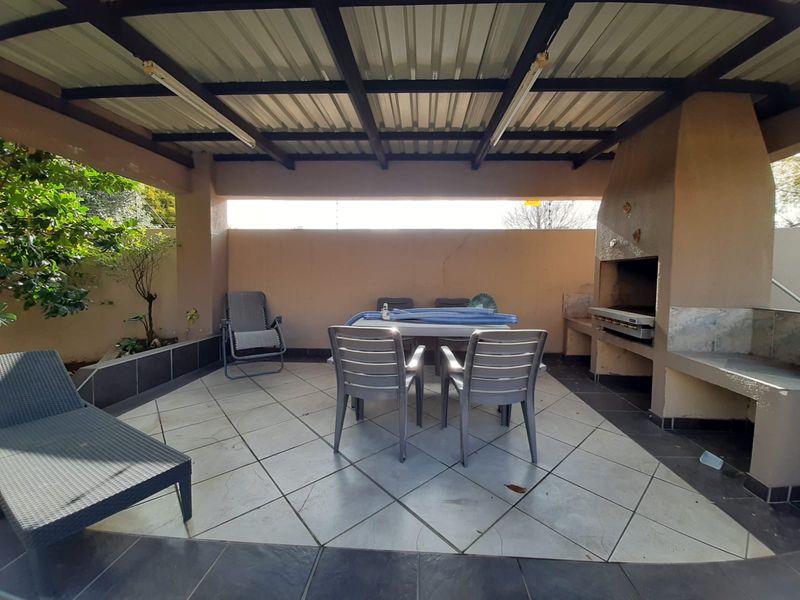Covered outdoor patio featuring a built-in braai, tiled flooring, and a corrugated metal roof structure, ideal for outdoor entertaining.