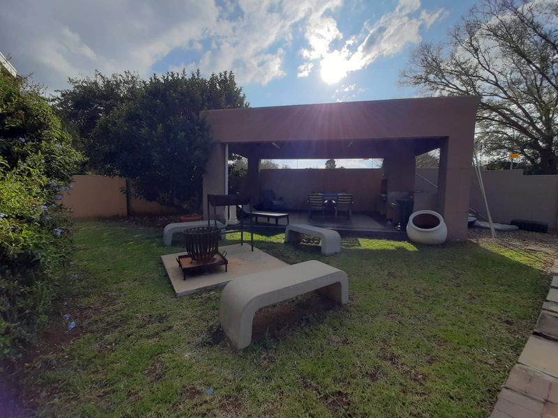Outdoor entertainment area featuring a covered patio with a built-in braai, concrete seating, and a landscaped garden setting.