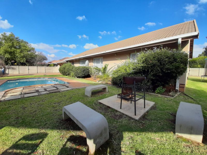 Rear garden area featuring a swimming pool, concrete seating, and a built-in braai area, set against the rear elevation of the house.