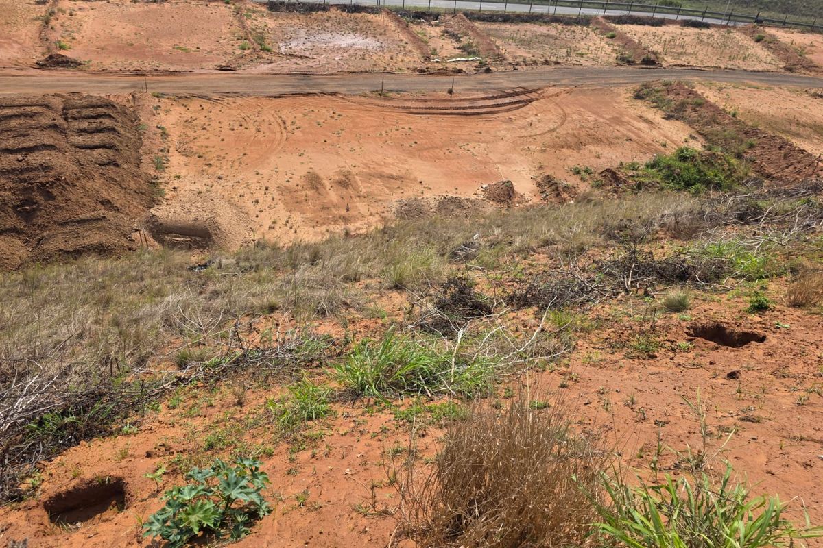 An elevated view of a vacant residential plot featuring graded earth, natural vegetation, and access to a nearby road.