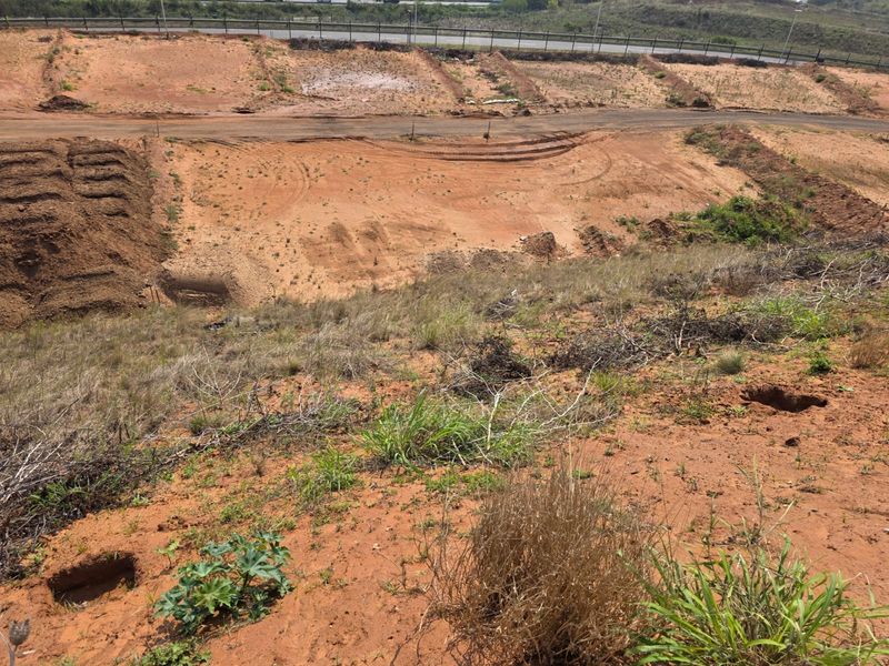 An elevated view of a vacant residential plot featuring graded earth, natural vegetation, and access to a nearby road.