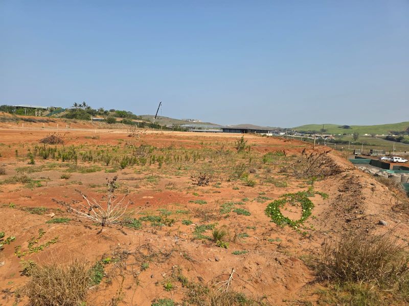 A wide-angle view of a vacant residential plot featuring cleared earth and natural landscape, ready for development.