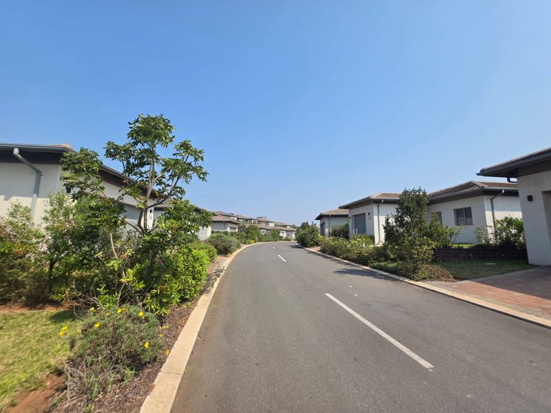 A view of the residential street within the estate, featuring paved roads, landscaped verges, and surrounding residential properties.