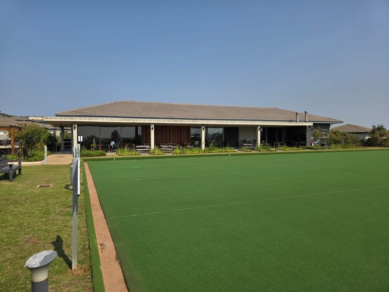 A well-maintained bowling green adjacent to a modern clubhouse featuring a covered patio and large sliding glass doors.