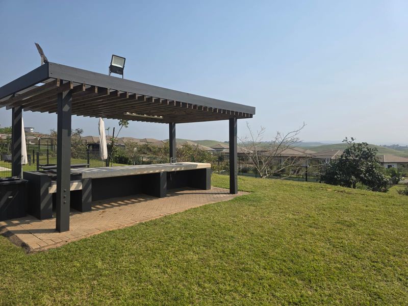 A covered outdoor entertainment area featuring a built-in braai, sink, and pergola, set within a landscaped garden with scenic views.