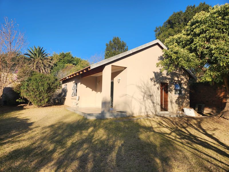 Rear view of the property featuring a covered patio area, established garden, and neutral exterior wall finish.