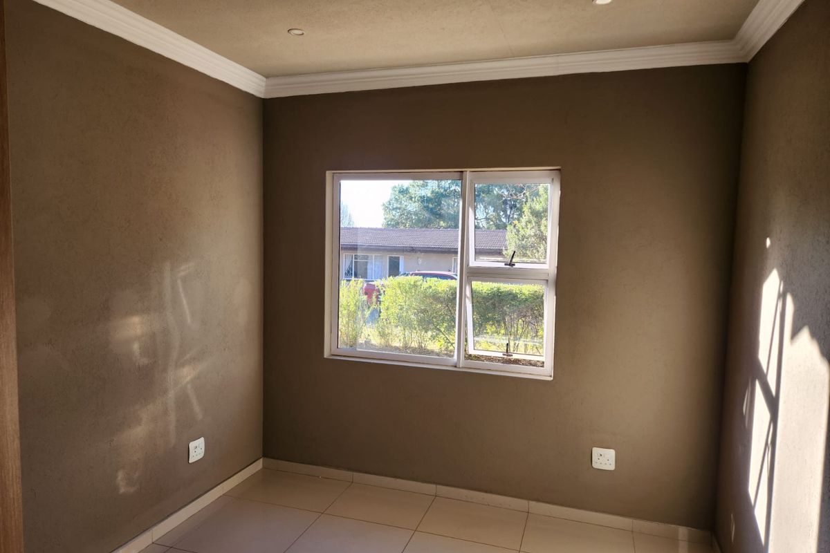 An empty bedroom featuring tiled flooring, recessed downlights, and a sliding window with a view of the exterior garden area.