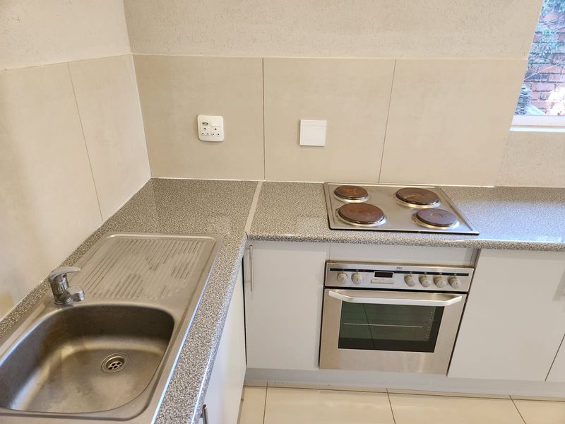 A clean, functional kitchen area featuring a stainless steel sink, laminate countertops, and a built-in electric oven with a four-plate hob.