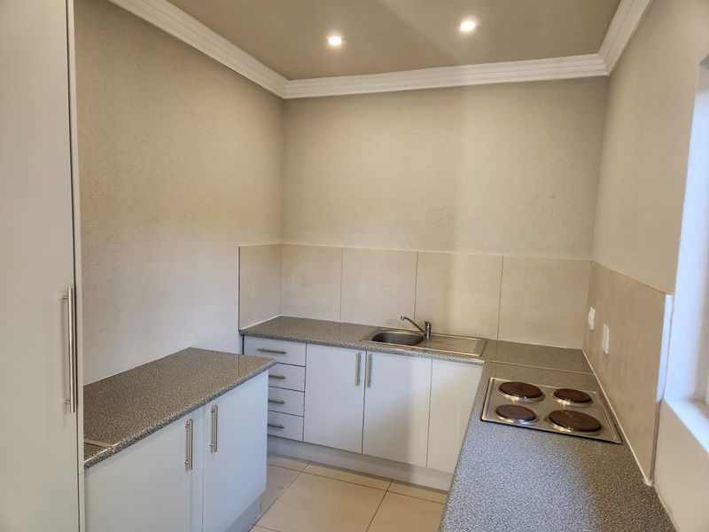 A clean, functional kitchen featuring laminate countertops, a built-in electric hob, stainless steel sink, and ample built-in cabinetry with neutral tiled splashbacks.