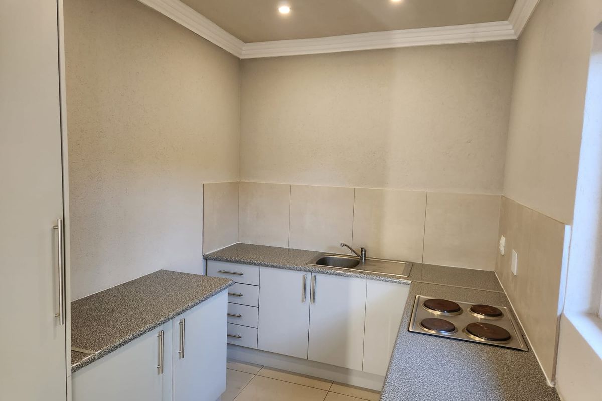 A clean, functional kitchen featuring laminate countertops, a built-in electric hob, stainless steel sink, and ample built-in cabinetry with neutral tiled splashbacks.
