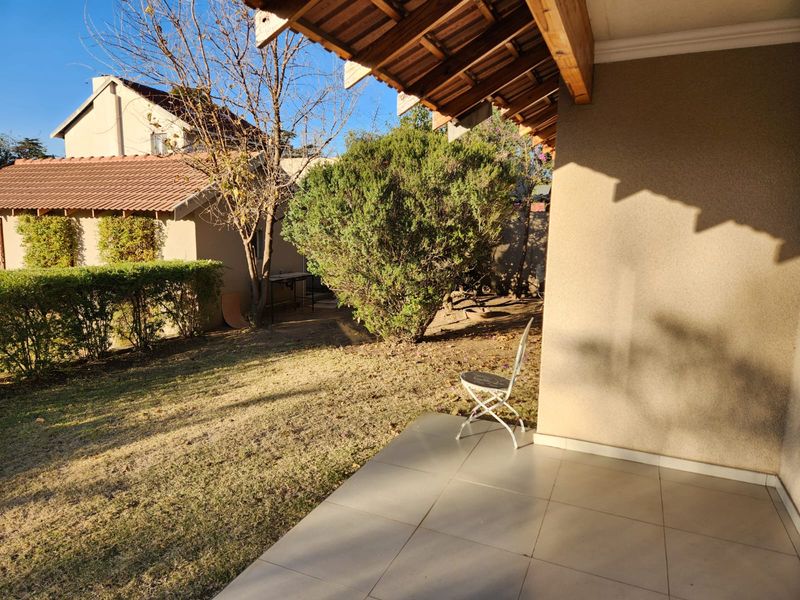 A covered patio area with tiled flooring and exposed timber rafters, overlooking a private garden space.