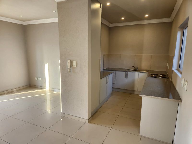 Modern open-plan kitchen and living area featuring neutral tiled flooring, built-in cabinetry with stone countertops, and integrated electric hob.