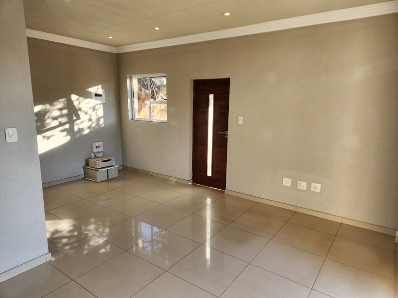 A bright, open-plan living area featuring neutral wall finishes, polished floor tiles, recessed lighting, and a modern timber entrance door.