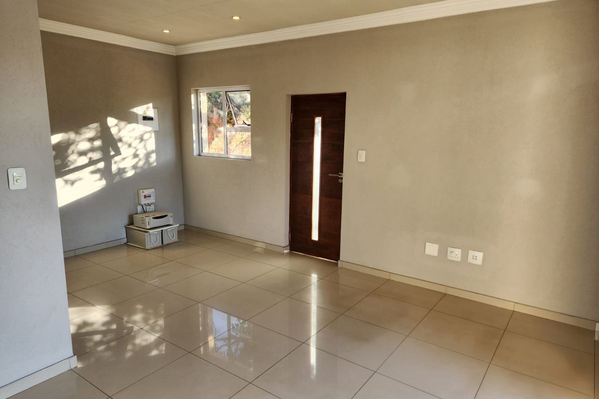 A bright, open-plan living area featuring neutral wall finishes, polished floor tiles, recessed lighting, and a modern timber entrance door.