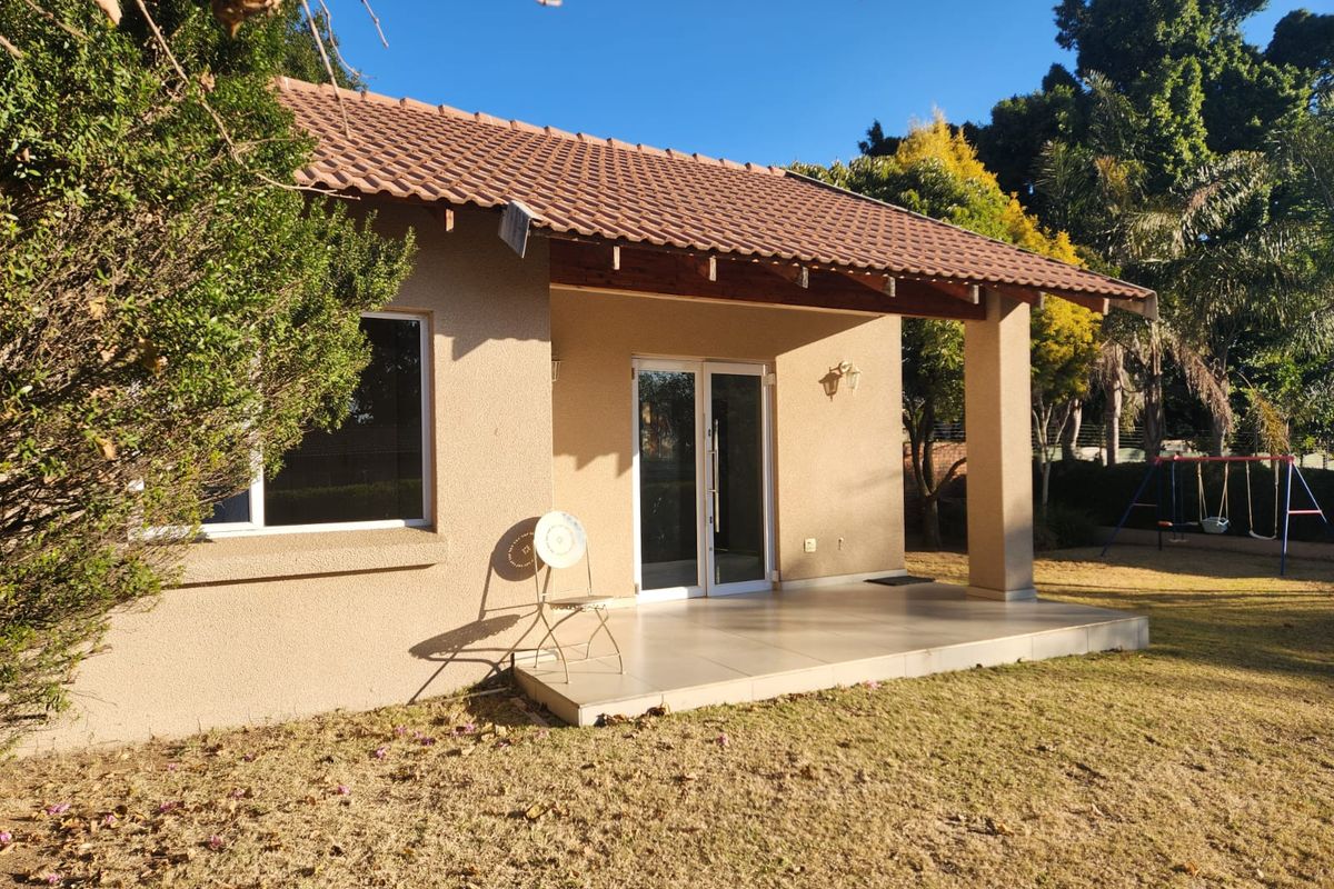 A rear view of the property featuring a covered tiled patio, sliding glass doors, and a well-maintained garden area.
