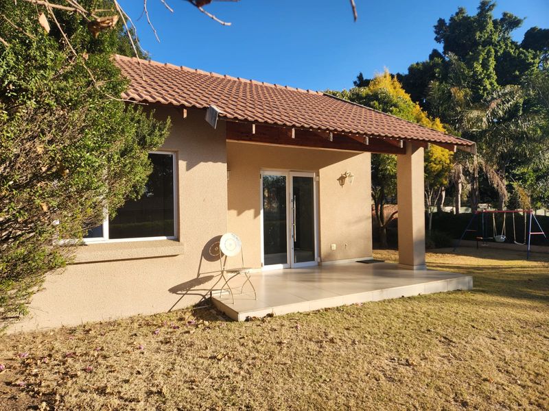 A rear view of the property featuring a covered tiled patio, sliding glass doors, and a well-maintained garden area.