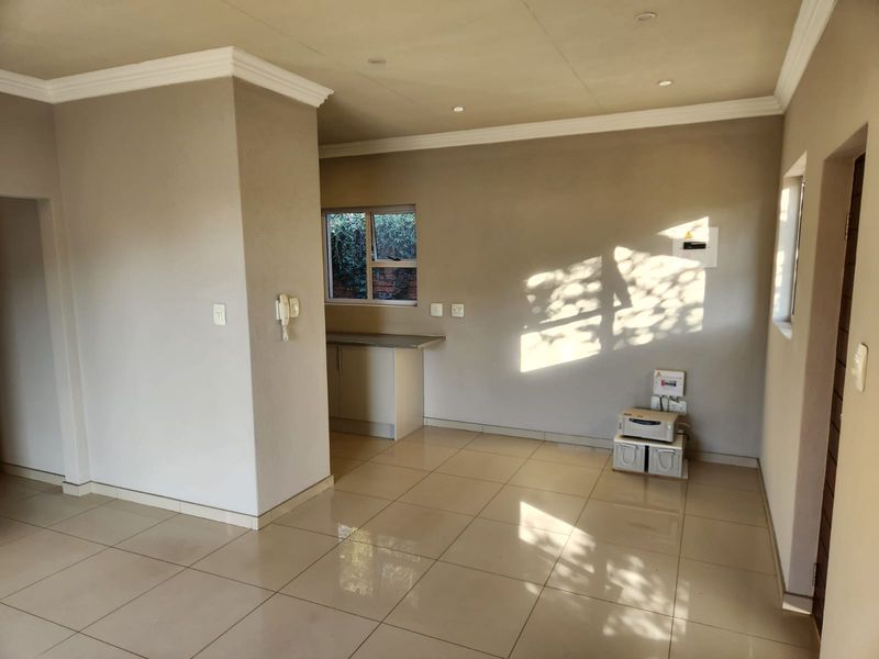 An open-plan living area featuring neutral tiled flooring, cornicing, and a compact kitchen counter section with natural light.
