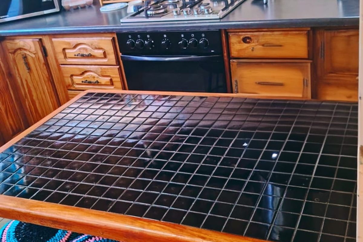 A functional kitchen featuring wooden cabinetry, a gas hob with extractor fan, and a central tiled island providing additional workspace.